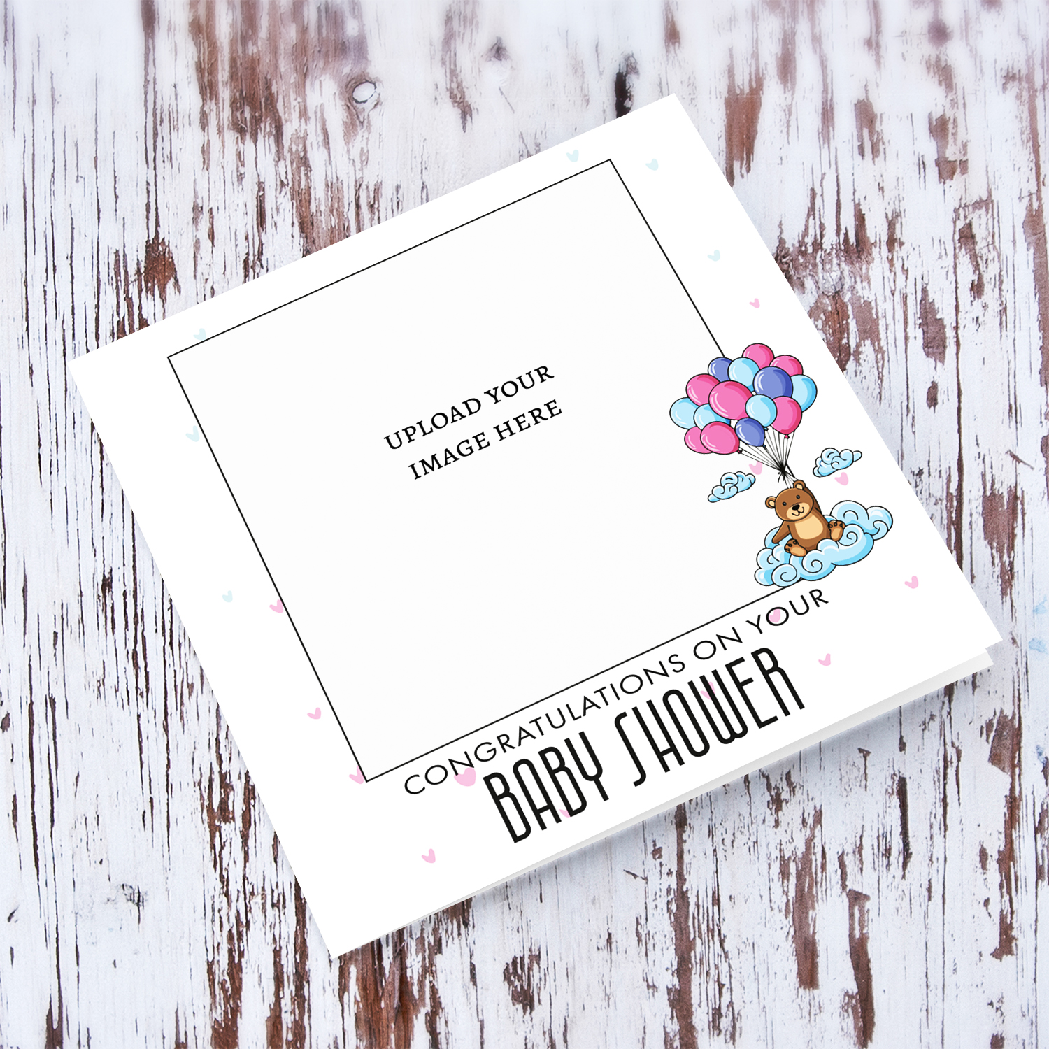 A cute bear holding blue, pink and purple balloons photo baby shower card with scattered hearts in English