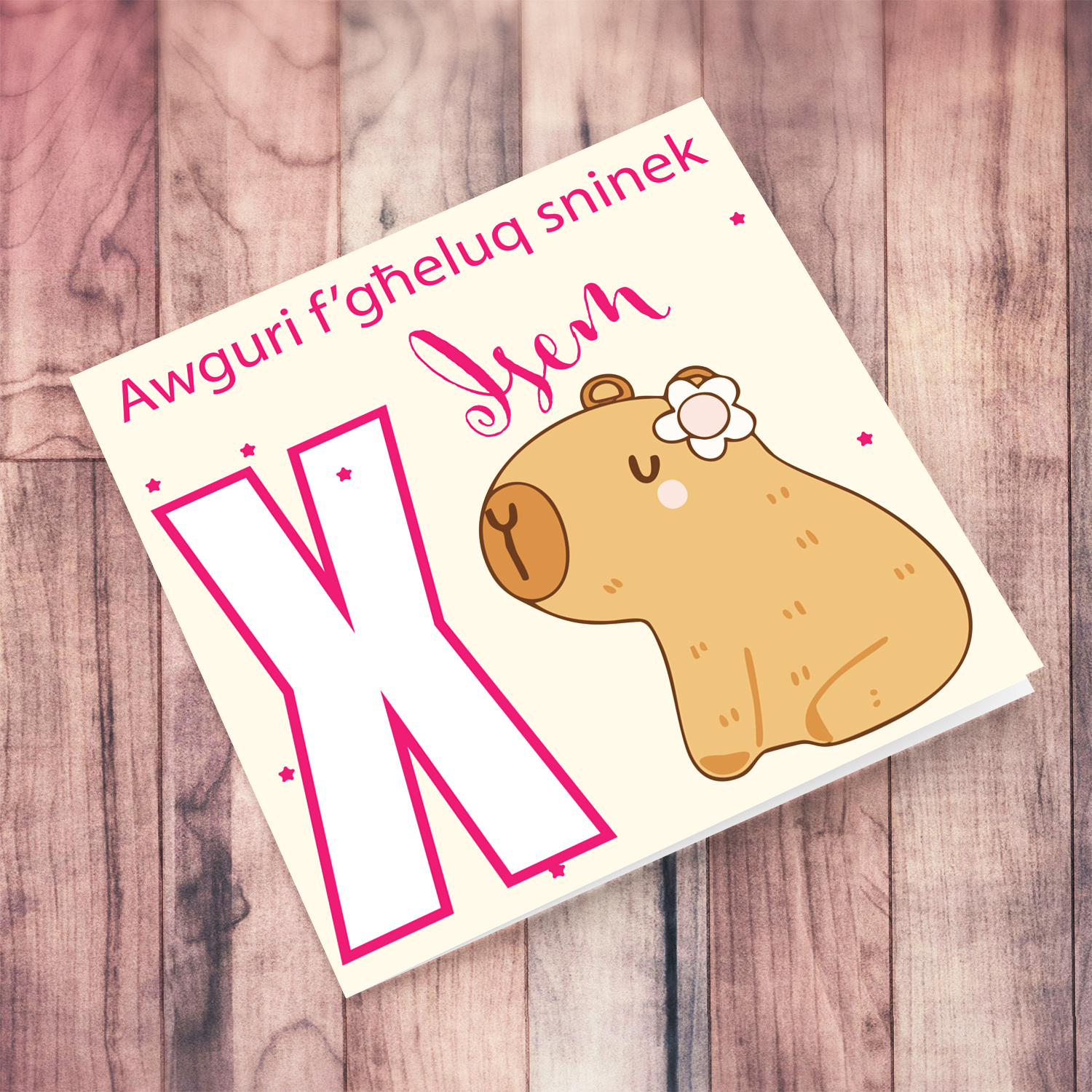 A cute birthday card featuring a capybara wearing a flower, personalisable with name and age in pink tones in Maltese (Personalisable + Enter Age)