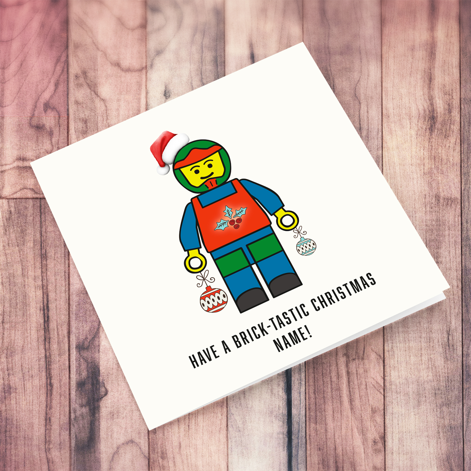 Cute Christmas card, featuring a lego mini figure wearing a santa hat and holding baubles in hands in English (Personalisable) 