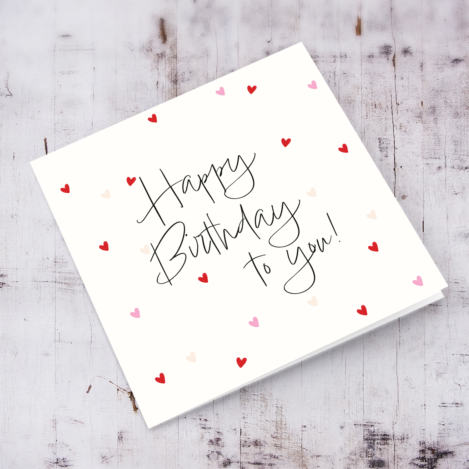 A cream coloured birthday card with scattered red and pink hearts in English
