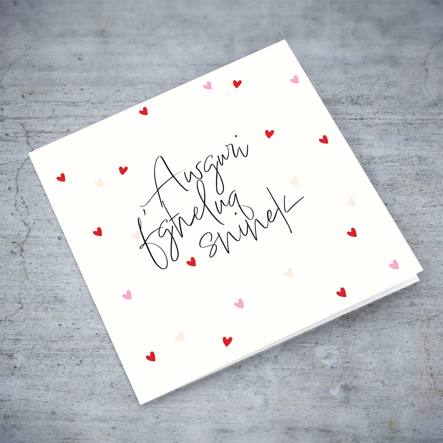 A cream coloured birthday card with scattered red and pink hearts in Maltese