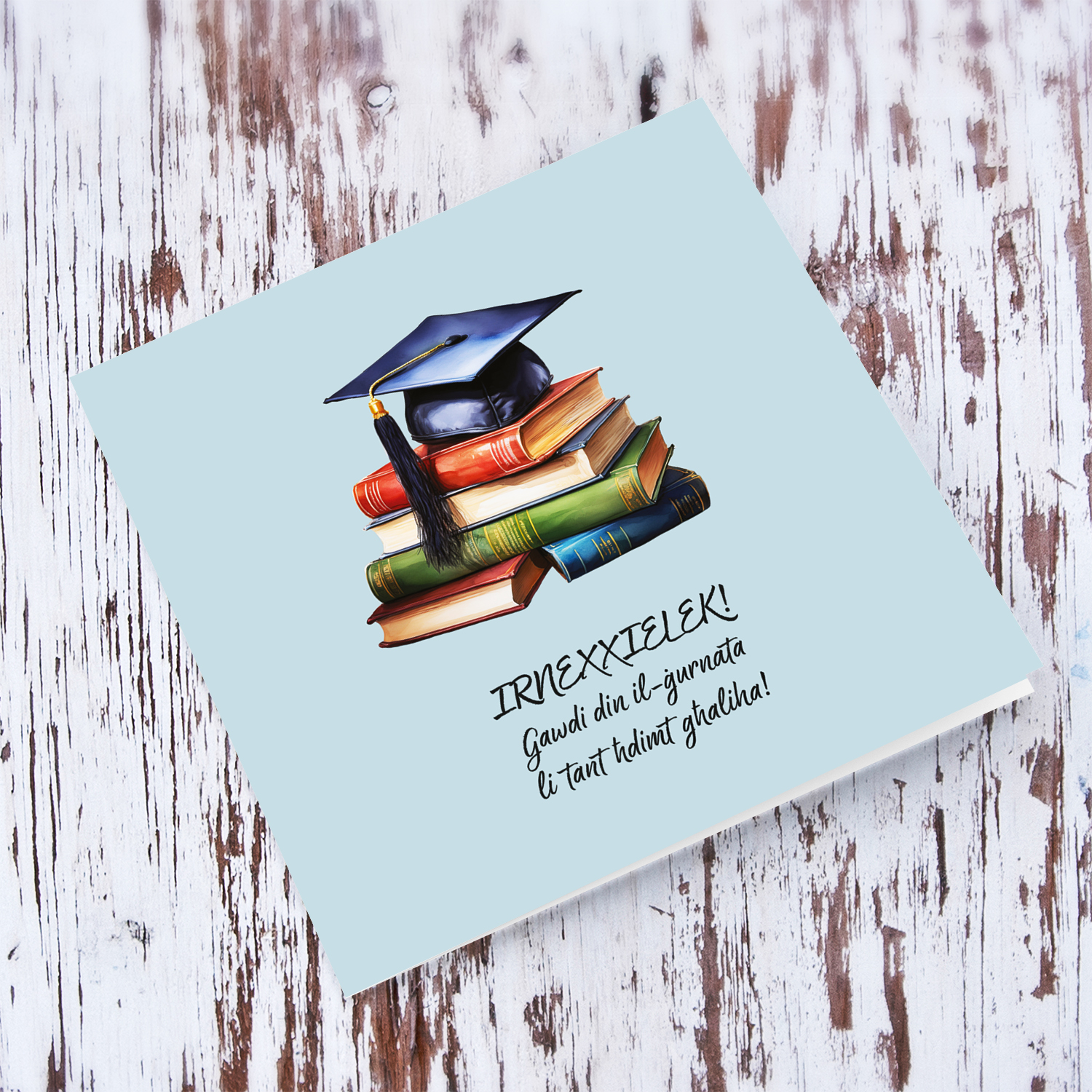A graduation card featuring a graduation hat sitting on a stack of books, in blue background in Maltese